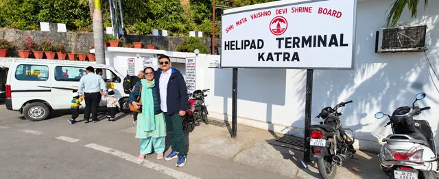 Travellers beside the Katra helipad terminal sign